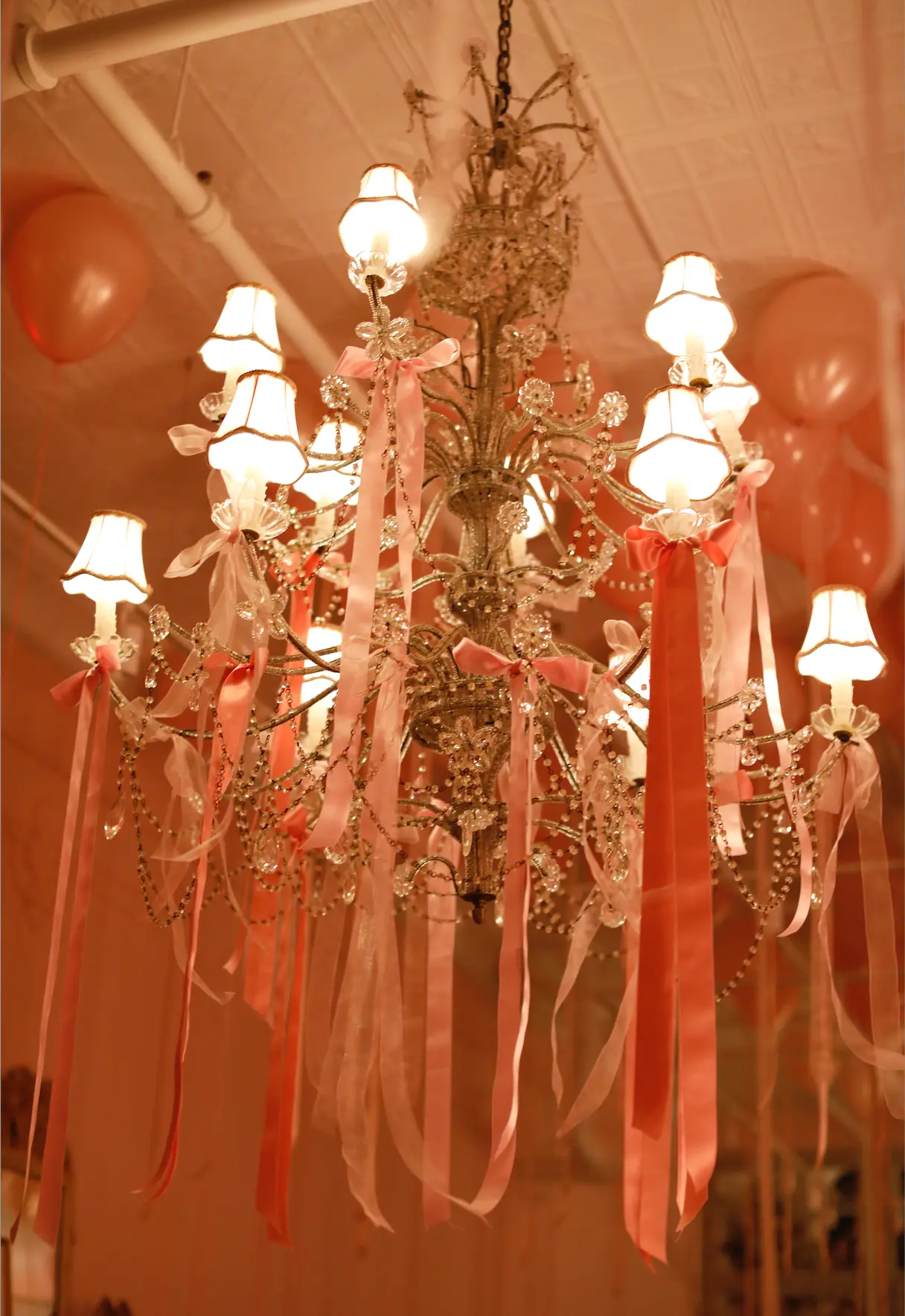 A crystal chandelier decorated with pink ribbons at a Love Shack Fancy event