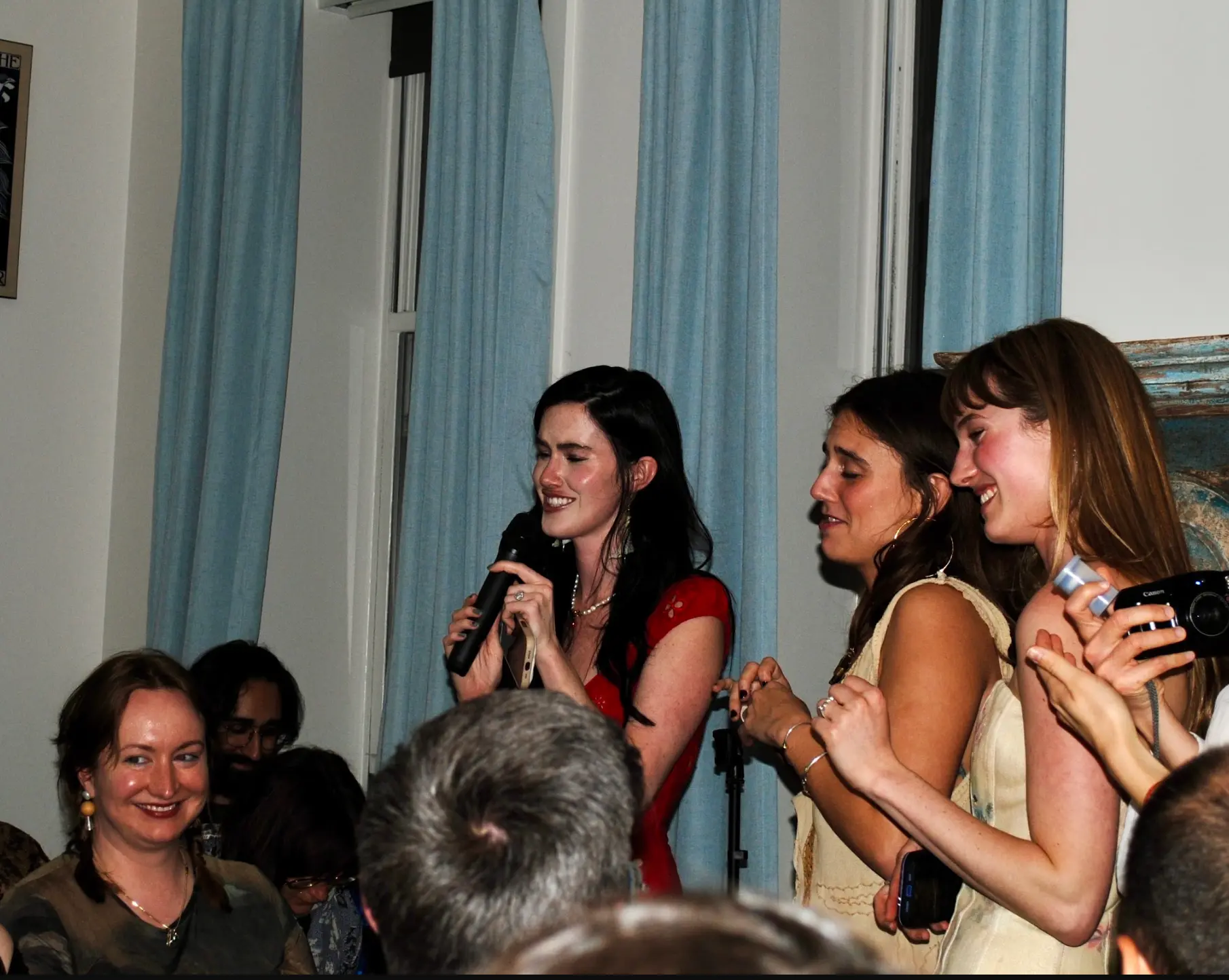 Three women laughing and speaking into a microphone at a reading